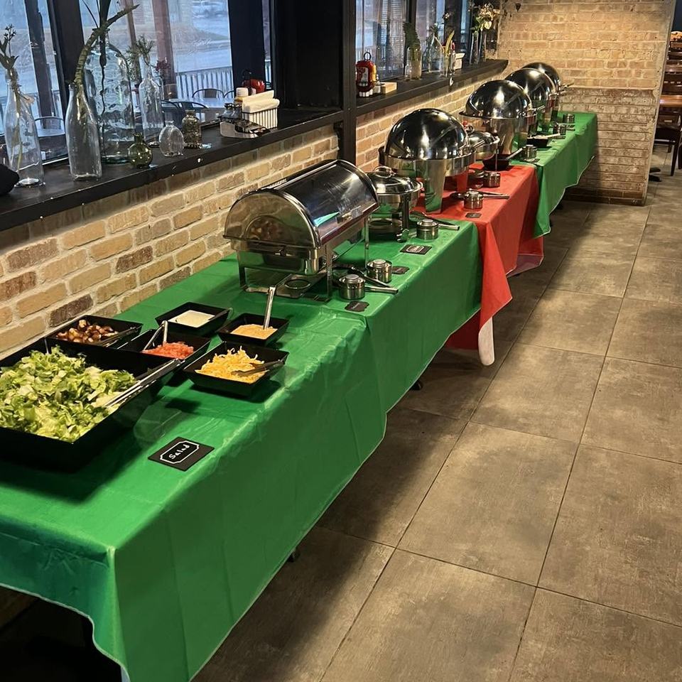 A long buffet of chafing dishes and salad bar on green and red tablecloths beside the dining-room windows.