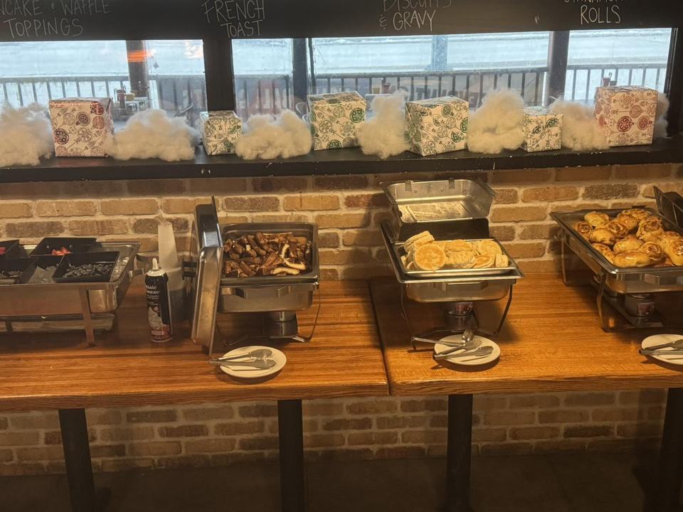 A brunch buffet of chafing dishes on a wooden counter against a brick wall.
