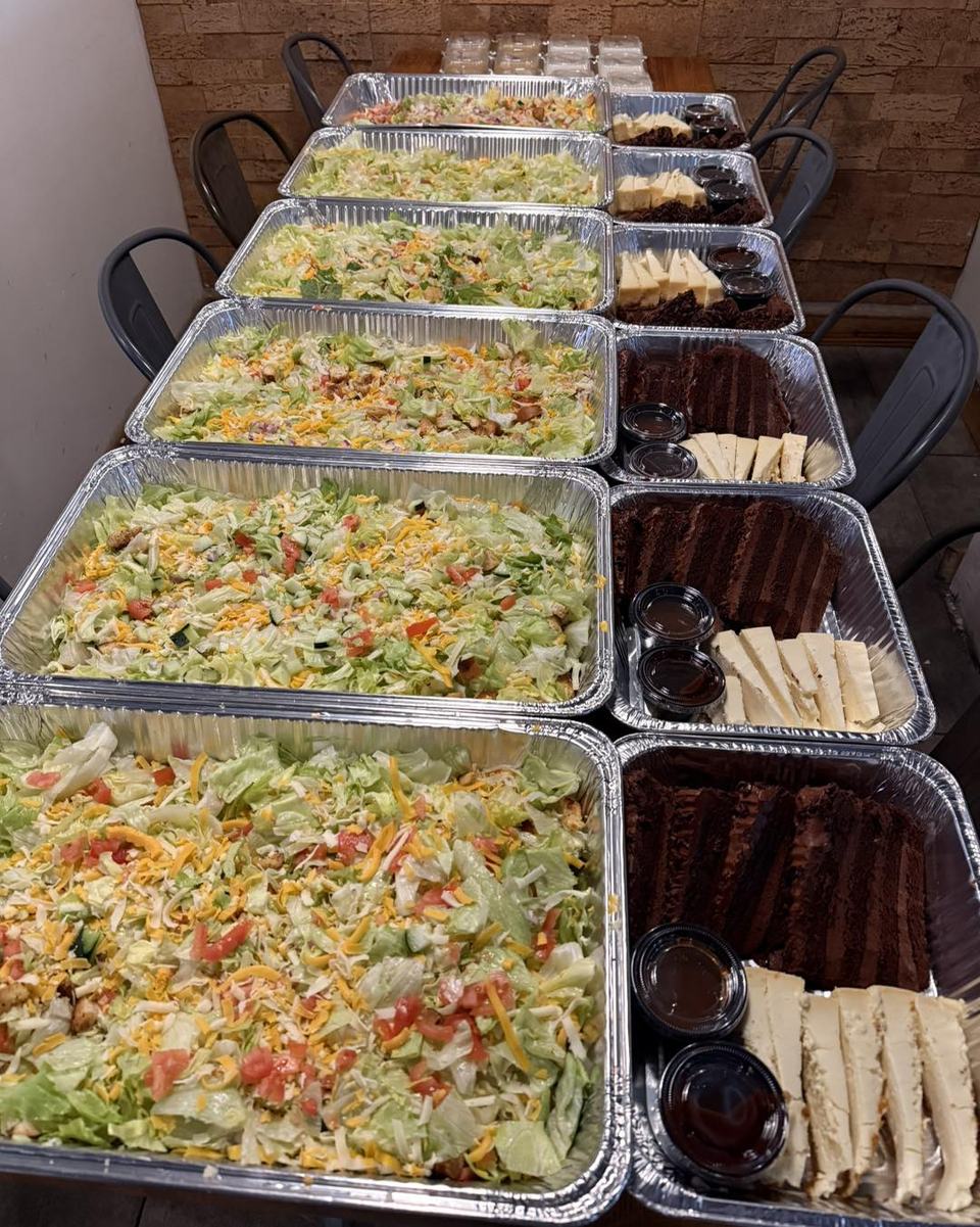 Rows of foil catering pans loaded with salad and sides on a long table.