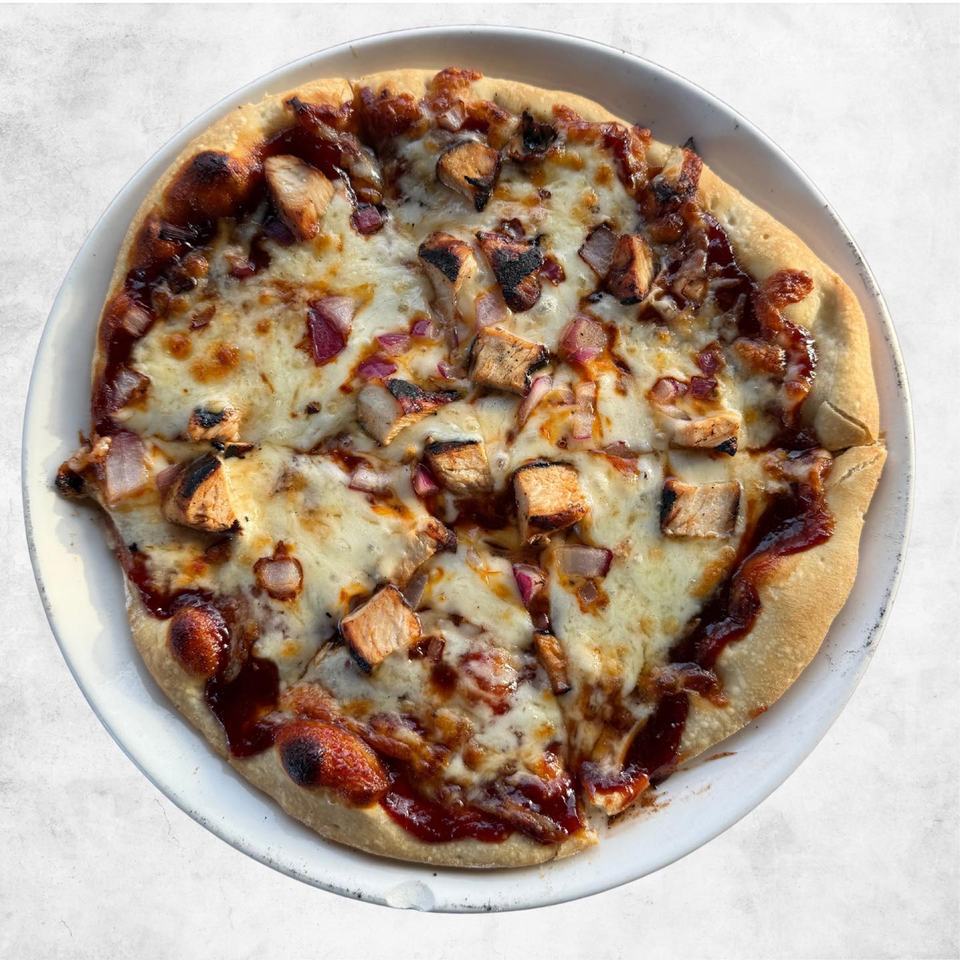 A BBQ chicken pizza with chicken pieces, onions and cilantro on a white background.
