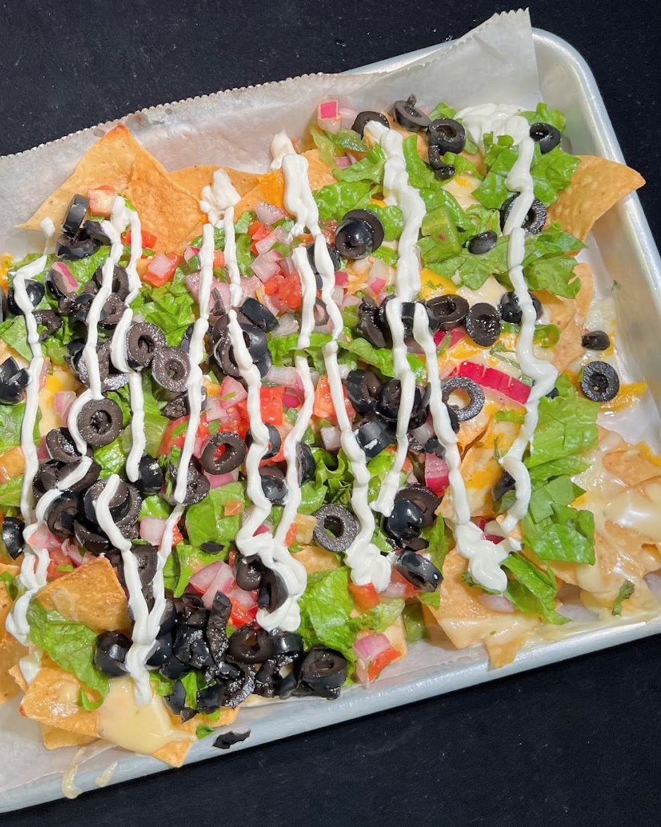 Layered nachos on a paper-lined tray: tortilla chips under black olives, lettuce, cheese and a zigzag of sour cream.