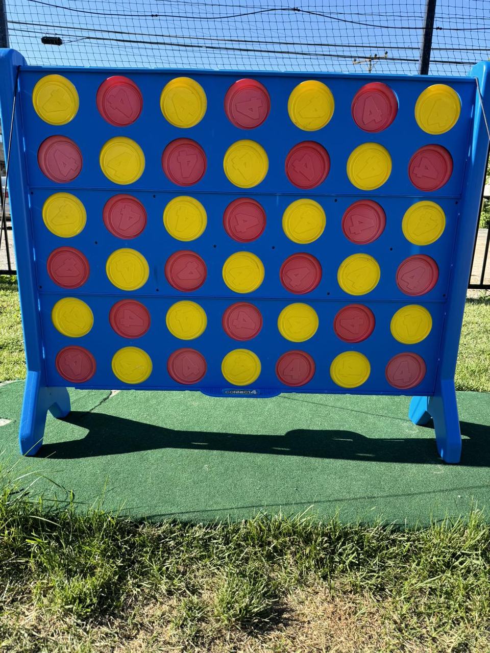 A giant Connect 4 game with red and yellow discs on the outdoor turf court.