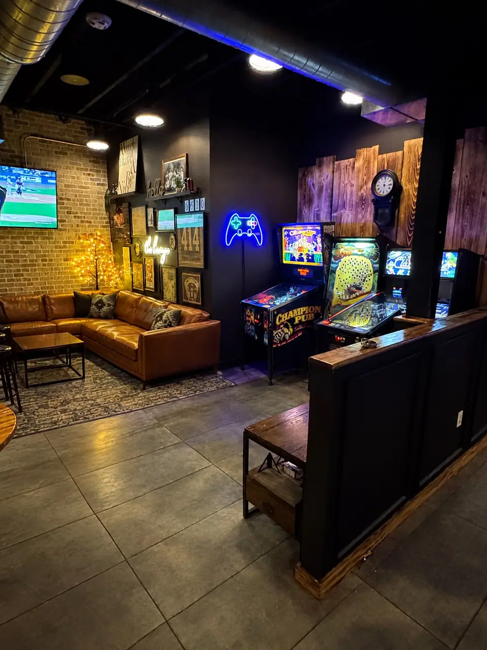 The lounge sectional beside a row of pinball and arcade games under a neon controller sign.