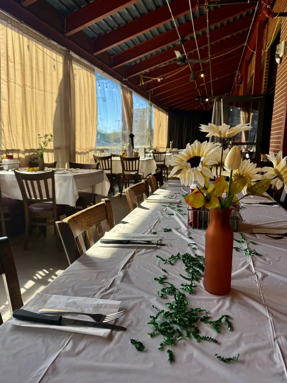 Close view of a patio party table: white cloth, place settings and a vase of sunflowers.