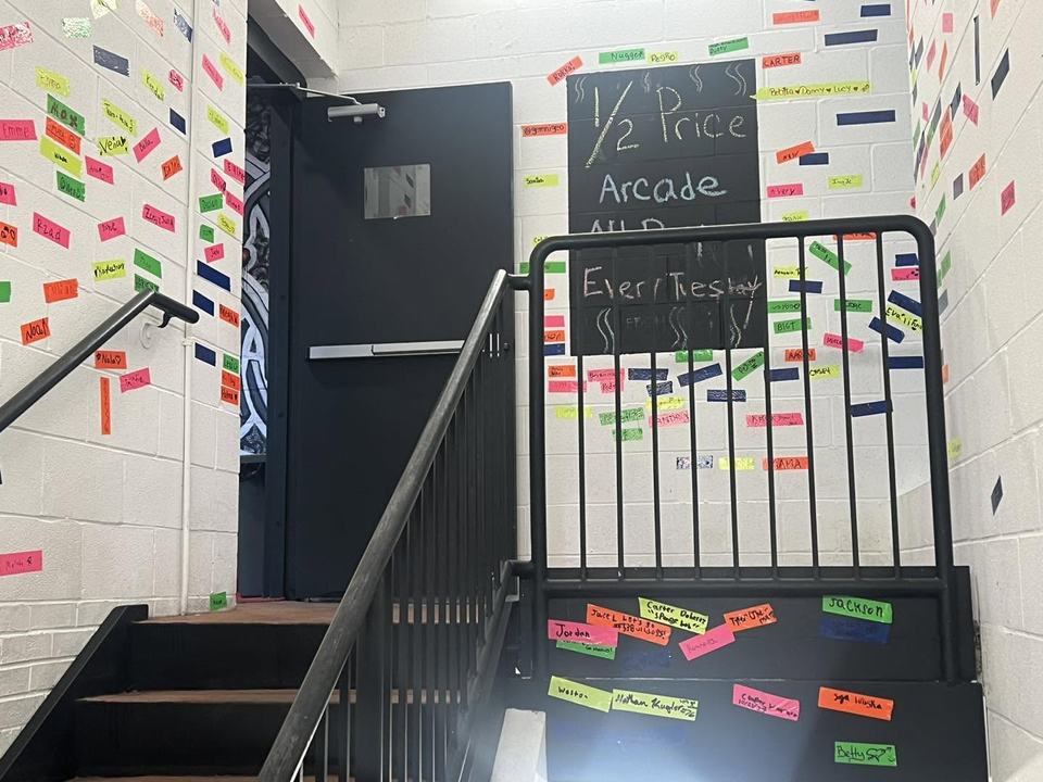 The stairwell wall covered in colored duct tape strips written on with guests' names, beside a chalkboard sign.